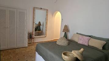 A bedroom with a bed, pillows, a lamp, a mirror, and a wardrobe.