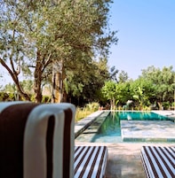 Zona de piscina con sillones de descanso y vistas a árboles.