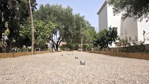 A courtyard with a gravel surface, trees, and a building in the background.