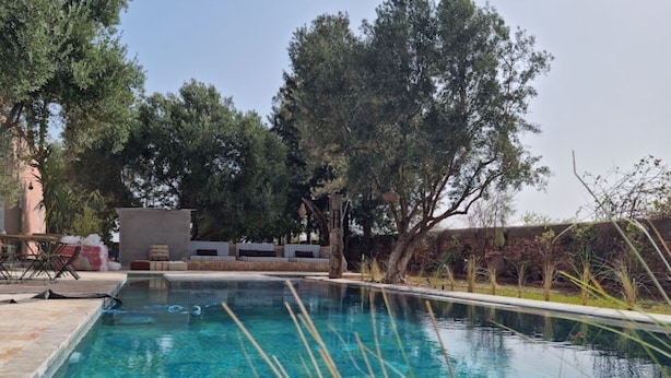 Una piscina exterior con agua cristalina, rodeada de árboles y un patio con mobiliario de exterior.
