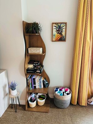 Een hoekzaal met een houten boekenkast, een schilderij van een ananas in een lijst, een kleine potplant en een gevlochten mand.