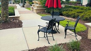 Eine Terrasse mit Sitzgelegenheiten im Freien, Palmen und einem Gebäude mit Balkonen.