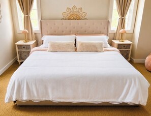 A large bed with a tufted headboard, two bedside tables with lamps, and a decorative wall piece. - Delilah's Hideaway : Cozy loft at Ste Augustine fully equiped for families (St. Augustine)