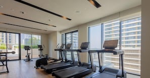 Ein modernes Fitnessstudio mit Laufbändern, Ergometer und Rudergerät. Große Fenster bieten Blick auf eine Stadtlandschaft.