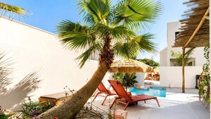 A poolside area with lounge chairs, a palm tree, and a thatched umbrella. - La Dolce Villa | Villa 5 étoiles, piscine chauffée, 700 m plage (Sérignan)