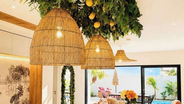 A modern kitchen with a central island, a dining area with a round table, and a view of an outdoor pool area. - La Dolce Villa | Villa 5 étoiles, piscine chauffée, 700 m plage (Sérignan)