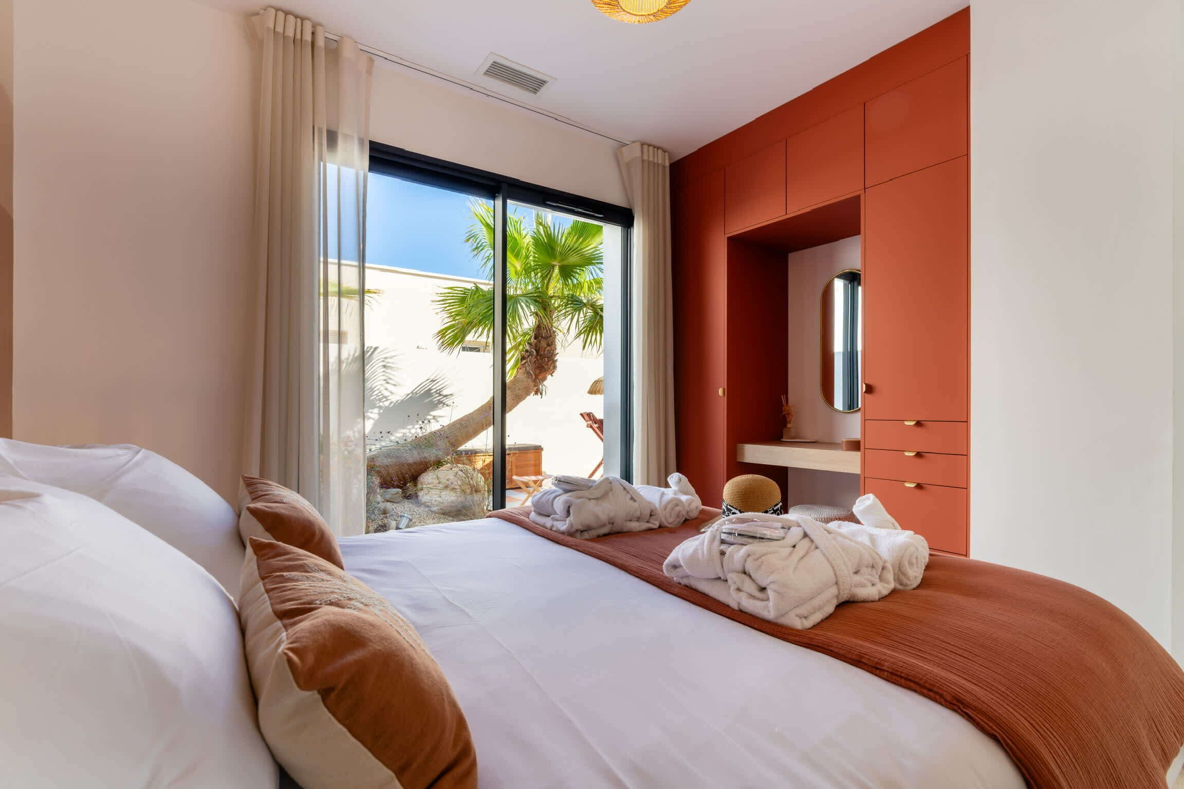 A hotel room with a bed, a bathroom with a mirror, and a view of palm trees.