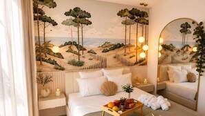 A bedroom with a bed, bedside tables, a tray with fruits and towels, a beach mural, and a large mirror. - La Dolce Villa | Villa 5 étoiles, piscine chauffée, 700 m plage (Sérignan)