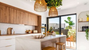 A modern kitchen with wooden cabinets, a marble countertop, a central island with stools, and hanging wicker lights. - La Dolce Villa | Villa 5 étoiles, piscine chauffée, 700 m plage (Sérignan)