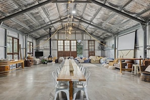 A spacious hall with a long wooden table and chairs, large windows, and a high ceiling with insulation. - Glen Eden Estate - Entire Estate (Broke)