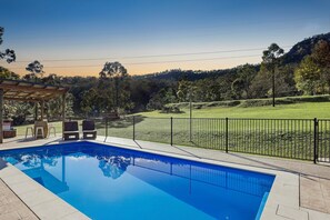 A swimming pool with a pergola and lounge chairs, surrounded by a fenced area and a view of a hilly landscape. - Glen Eden Estate - Entire Estate (Broke)