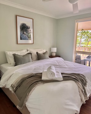 A neatly made bed with a rolled towel, a framed picture on the wall, and a window with a view of greenery. - Glen Eden Estate - Entire Estate (Broke)