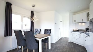Et moderne køkken med hvide skabe, et spiseområde med et træbord og sorte stole, samt en gulv belagt med gråt træ.