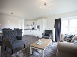 A modern living room with grey upholstered chairs, a wooden coffee table, and a grey sofa. A kitchen with white cabinets and a microwave is visible in the background. - Holiday Home in Nijkerk With Terrace (Nijkerk)