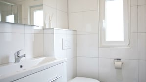 Et moderne badeværelse med hvid vask, spejl og toilet.
