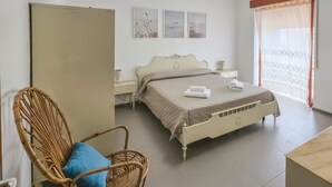 Ein Schlafzimmer mit einem Bett, einem Sessel, einem Nachttisch und einem Fenster mit Vorhängen.
