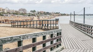 Ein Strand mit einem hölzernen Promenadenweg, Sonnenschirmen und sandigem Ufer.