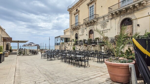 Ein Außenbereich mit Tischen und Stühlen, ein Gebäude mit der Aufschrift 'Murphy's Pub' und Blick auf das Meer.