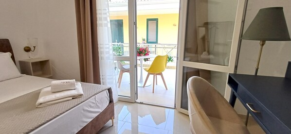 Ein Hotelzimmer mit Bett, Schreibtisch, Stuhl, Lampe und einem Balkon mit Tisch und Stühlen.