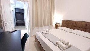 A hotel room with a bed, a desk, a chair, a wardrobe, and a nightstand with a lamp. - Vegan B&B (Syracuse)