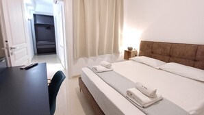 A hotel room with a bed, a desk, a chair, a nightstand with a lamp, and a closet. - Vegan B&B (Syracuse)