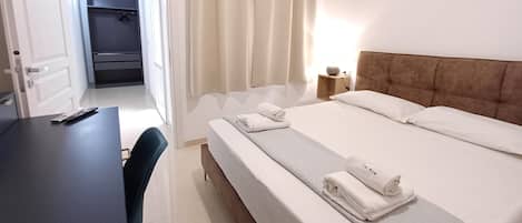 A hotel room with a bed, a desk, a chair, a nightstand with a lamp, and a closet.