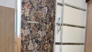 A shower with a floral wallpaper, a glass door, and a white towel on the floor. - Vegan B&B (Syracuse)
