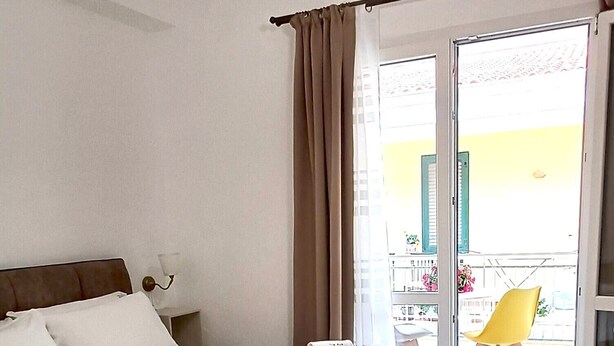 A hotel room with a bed, a bedside table, a lamp, a window with curtains, and a view of the outside. - Vegan B&B (Syracuse)
