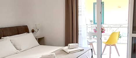 Habitación de hotel con cama, mesita de noche, lámpara, ventana con cortinas y vistas al exterior.