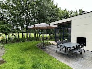 An outdoor patio with a table and chairs, a covered umbrella, and a modern building with large windows. - Holiday Home in Velsen-zuid With Terrace (Velsen-Zuid)