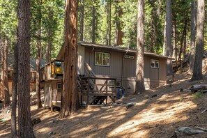 A cabin in a forest with a wooden deck and a small porch. - Bigfoot Escape | Dorrington Cabin with Bonus Room (Camp Connell)