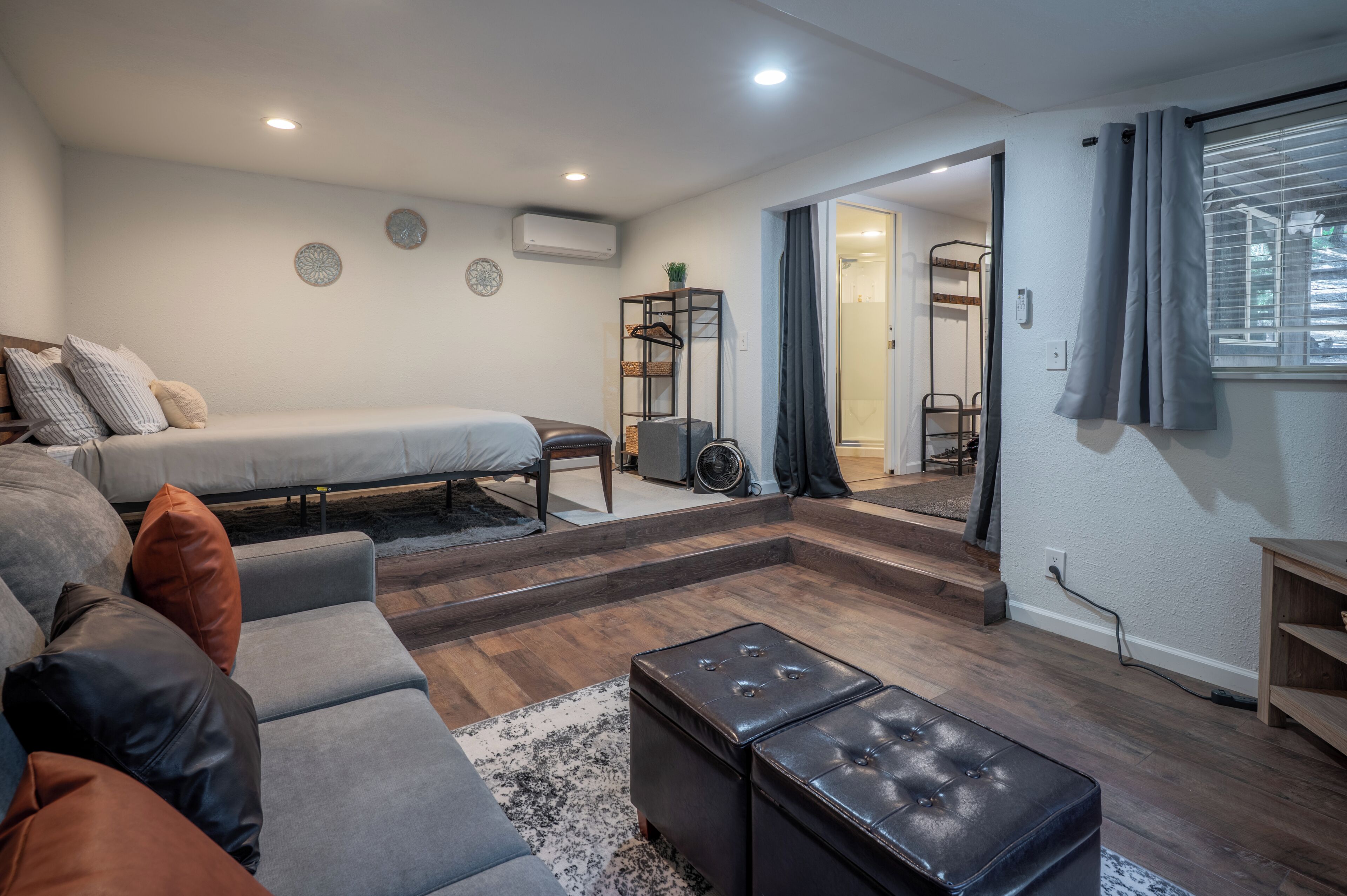 Un salon moderne avec un canapé, un pouf et un lit. On y trouve une petite table et une étagère sur laquelle sont posés divers objets.