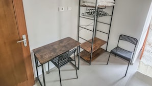 Una habitación de esquina con una mesa de madera, dos sillas, un estante metálico y una puerta.