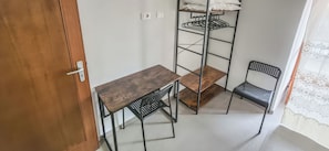 Una habitación de esquina con una mesa de madera, dos sillas, un estante metálico y una puerta.