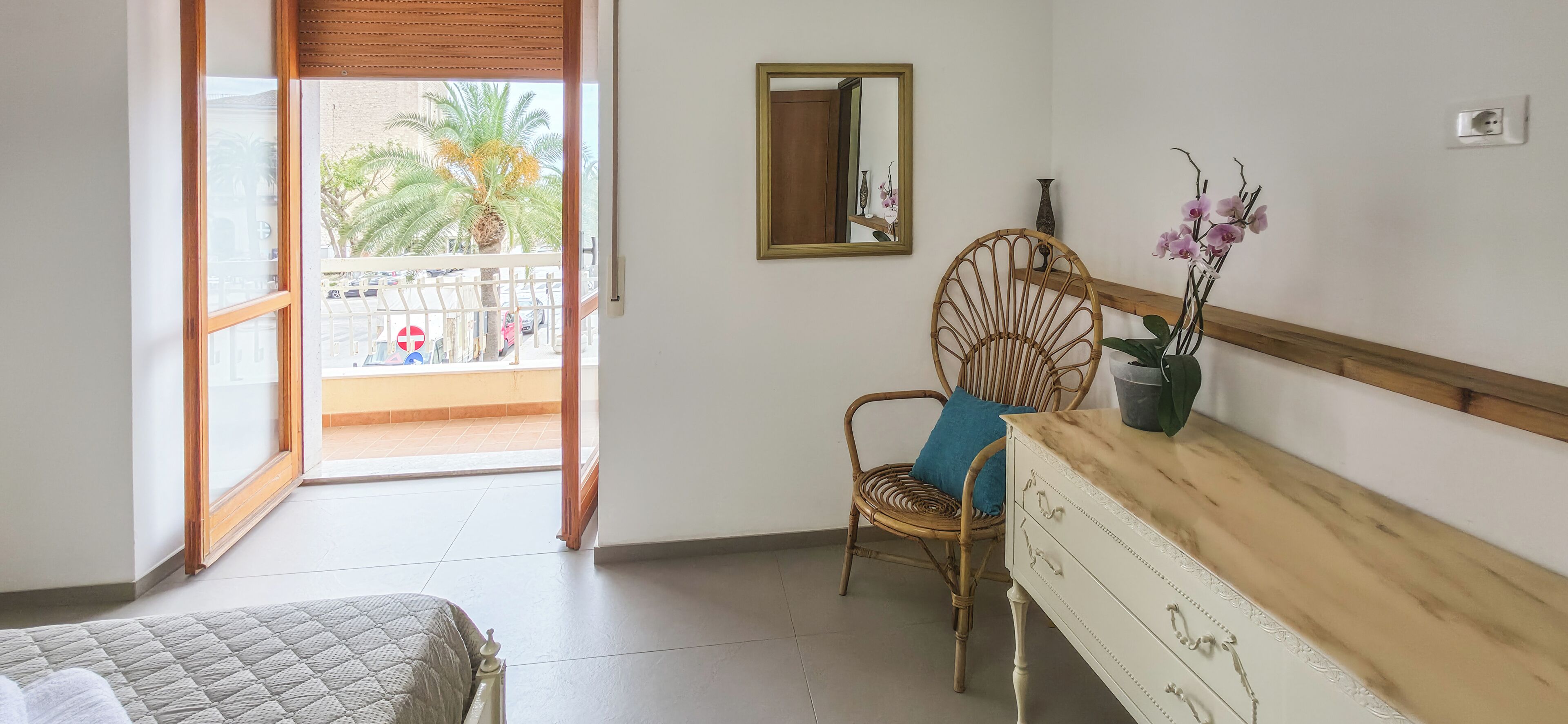 A room with a bed, a chair with a cushion, a dresser, a mirror, and a potted plant.