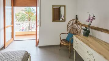 A room with a bed, a chair with a cushion, a dresser, a mirror, and a potted plant.