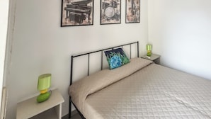 Un dormitorio con una cama, una mesita de noche, una lámpara y dos cuadros en la pared.