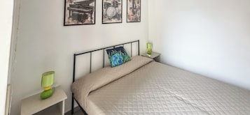 Un dormitorio con una cama, una mesita de noche, una lámpara y dos cuadros en la pared.
