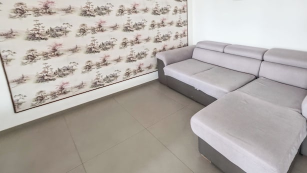 Una habitación con un sofá gris, suelo de baldosas y una pared con estampado floral.