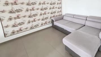 Una stanza con un divano grigio, pavimento piastrellato e una parete decorata con un motivo floreale.