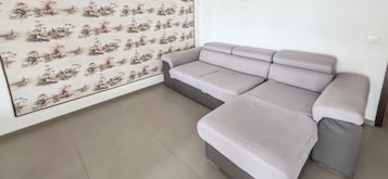 Una habitación con un sofá gris, suelo de baldosas y una pared con estampado floral.