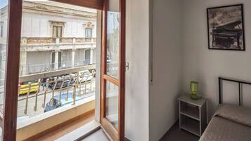 Une chambre avec un balcon, un lit, une table de chevet et des tableaux encadrés au mur.