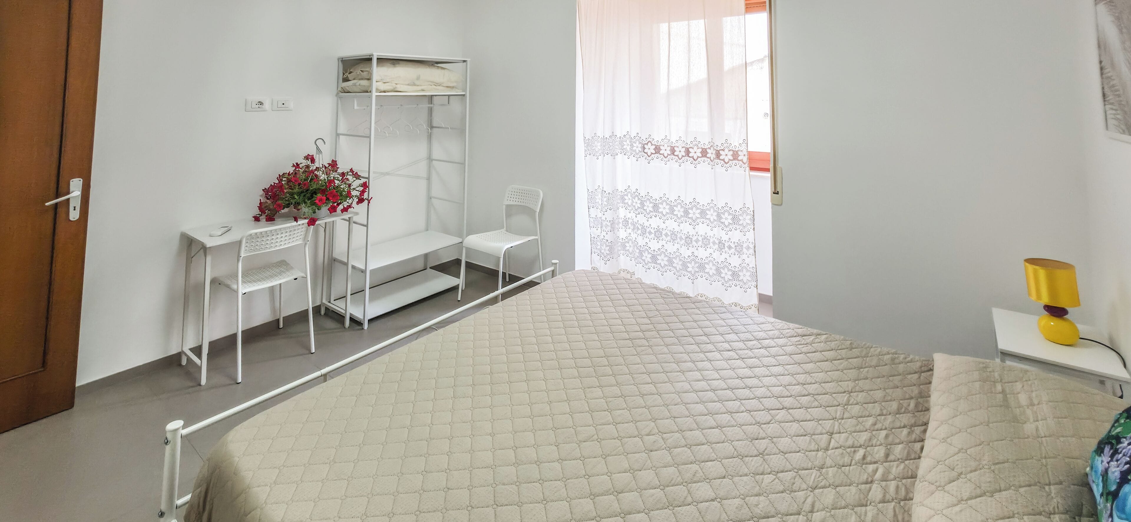 Ein Schlafzimmer mit einem Bett, einem Schreibtisch mit Stuhl, einem Kleiderschrank und einem Fenster mit Vorhang.