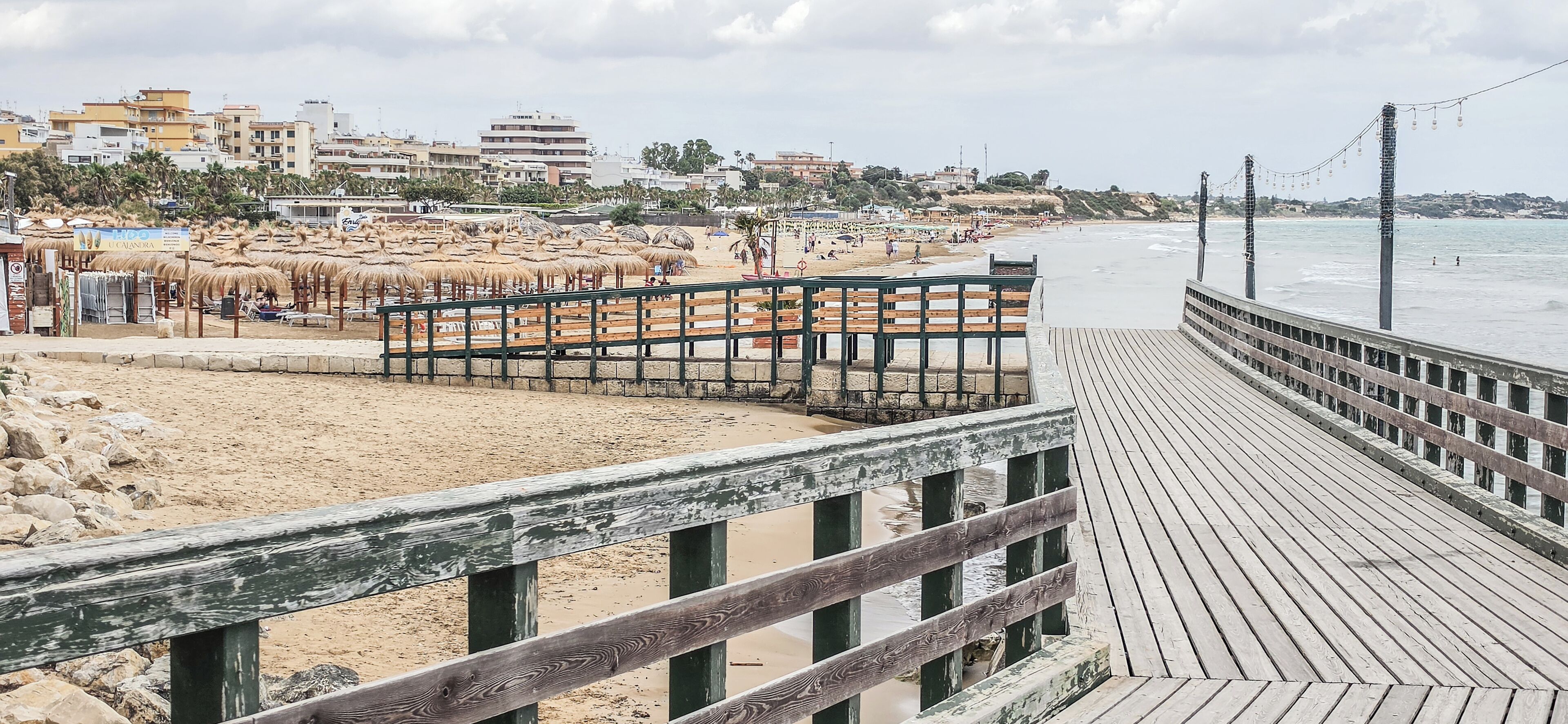 Une plage avec une promenade en bois, des parasols et des bâtiments en arrière-plan.