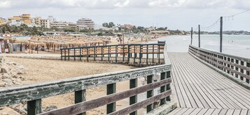 A beach with a wooden boardwalk, umbrellas, and buildings in the background.