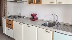 Una cocina compacta con estufa a gas, una cafetera roja, un lavamanos y armarios de madera.