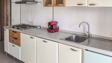 Una cucina compatta con piano cottura a gas, una macchina del caffè rossa, un lavello e pensili in legno.
