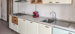 Una cocina compacta con estufa a gas, una cafetera roja, un lavamanos y armarios de madera.
