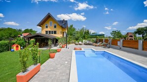 Una casa con piscina, area salotto esterna e spazio giochi.