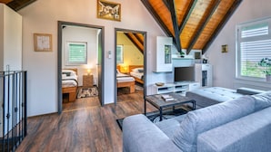 Un interno moderno con una camera da letto mansardata, una zona living con divano e televisione e una sala da pranzo con tavolo e sedie.
